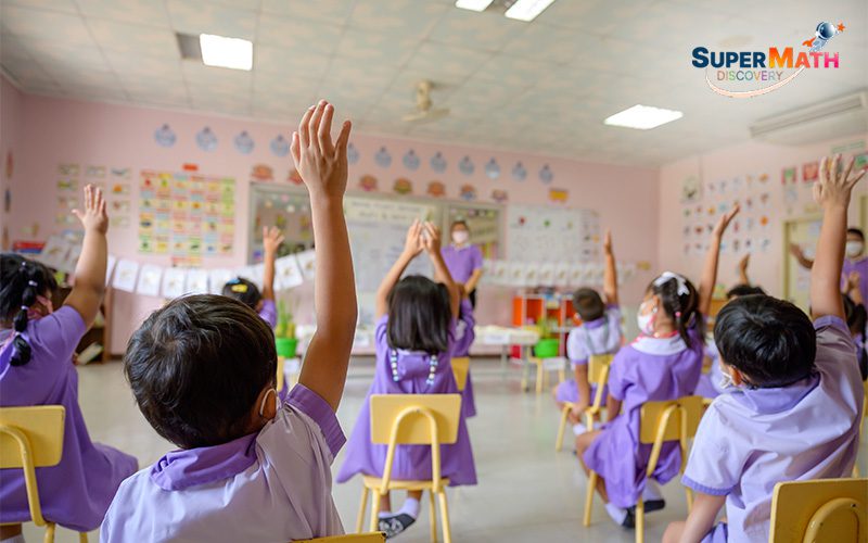 Preschool students raising their hands in class.