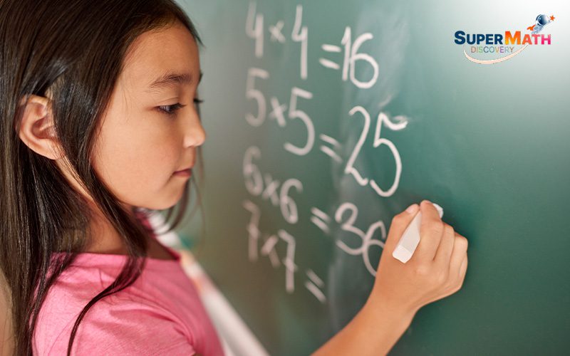 Student solving multiplication problems on a blackboard.